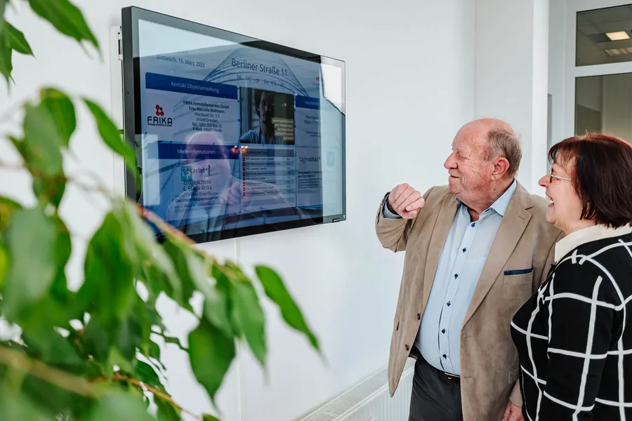Zwei Personen stehen vor einer digitalen Infotafel in einer Pflegeeinrichtung.